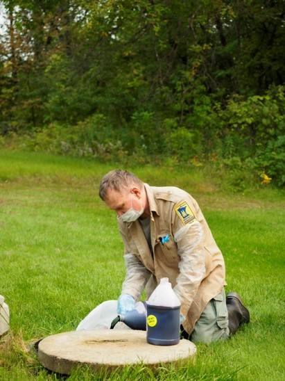 Photograph of Jeff Green wearing a DNR uniform and pouring dye into a well.
