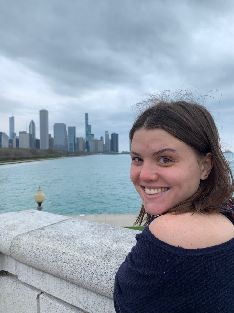 Photograph of Anna Klein wearing a blue sweater and posing by a body of water.