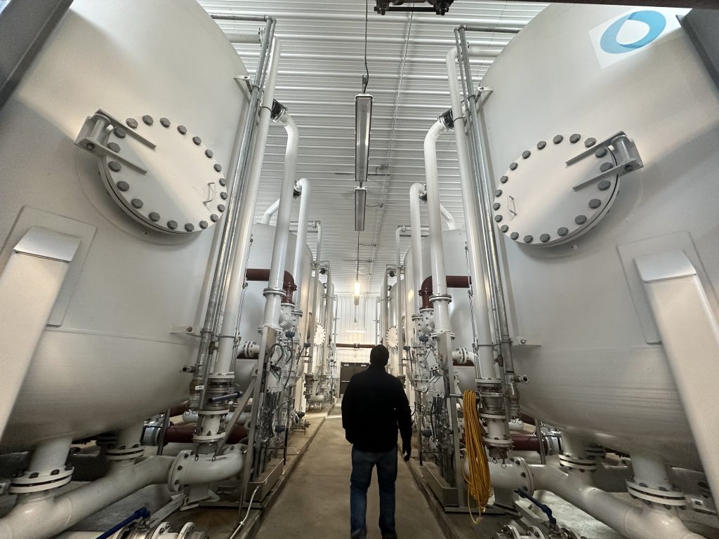 Photograph of a water treatment system. A man is shown next to the system to show the system is at least 10 feet tall.
