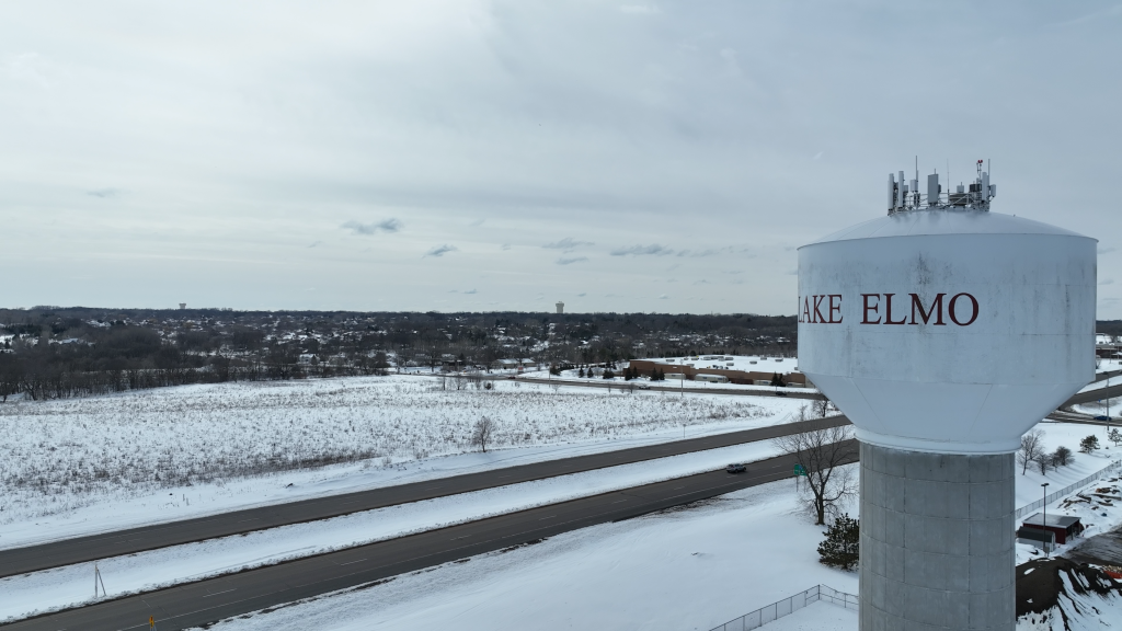 Photograph of the a water tower in the city of Lake Elmo, Minnesota and a snow-covered field near a roadway.