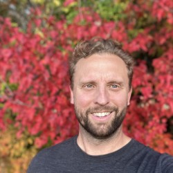 Photograph of Eric Bunge. The photograph is of his face, and he is in front of a background with red and yellow leaves.