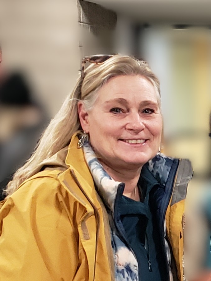 Photograph of Cathy Undem. Cathy has long hair and is wearing a yellow jacket.