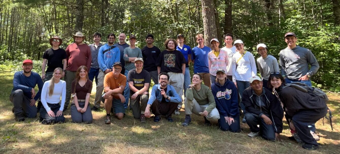 Photo of 2026 University of Minnesota Hydrogeology Field Camp attendees. There are 25 people standing in two rows in front of a forested background.